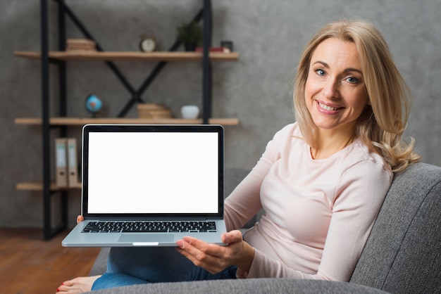 Glimlachende jonge vrouwenzitting op bank die haar laptop vertoning toont