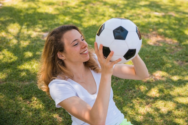 Glimlachende jonge vrouwenzitting op gras met voetbal