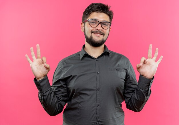 Glimlachende jonge zakenman die glazen draagt die mediterend gebaar tonen dat op roze wordt geïsoleerd