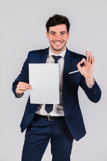 Glimlachende jonge zakenman die Witboek houdt in hand die ok teken toont