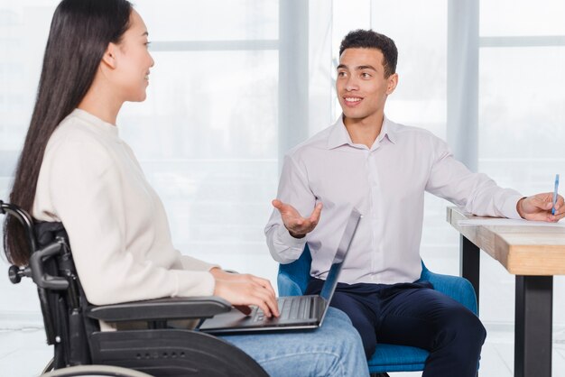 Glimlachende jonge zakenman en gehandicapte vrouw die bespreking in het bureau hebben