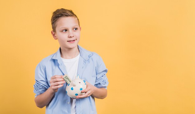 Glimlachende jongen die de muntnota opnemen in ceramische witte piggybank