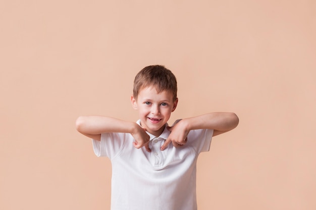 Glimlachende jongen die wijsvinger richten op zich die zich dichtbij beige muur bevinden