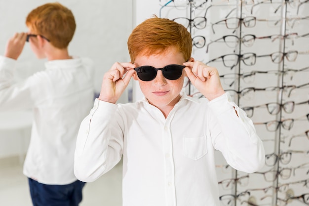 Glimlachende jongen die zwarte eyewear in optiekkliniek draagt