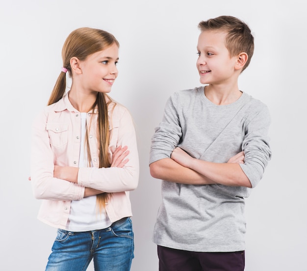 Glimlachende jongen en meisje met gekruiste wapens het kijken aan camera tegen witte achtergrond