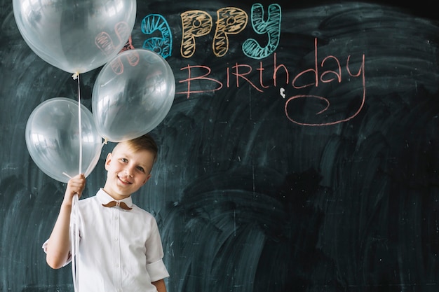 Gratis foto glimlachende jongen met ballons dichtbij het gelukkige verjaardag schrijven