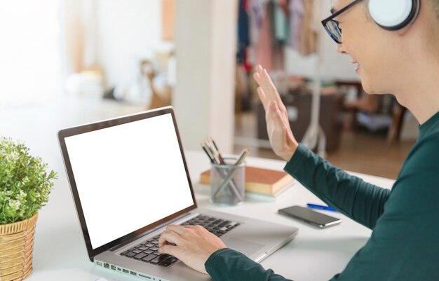 Glimlachende knappe Aziatische zakenman draagt een koptelefoon die op afstand werkt vanuit huis. Hij is webinar videoconferentie, Laptop leeg scherm.