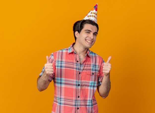 Glimlachende knappe blanke man met verjaardagspet duimen omhoog met twee handen