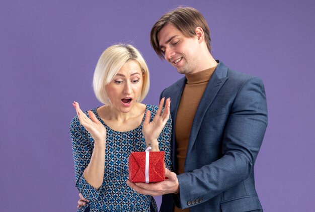 Glimlachende knappe slavische man die rode geschenkdoos geeft aan verraste mooie blonde vrouw op valentijnsdag