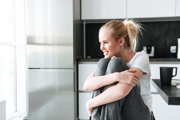 Glimlachende leuke dame die opzij kijken terwijl het zitten in keuken