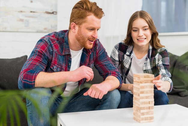 Glimlachende man die vrouw bekijken die thuis het spel van de houtsnedestapelstapel spelen