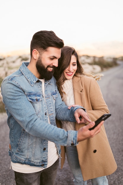 Glimlachende man en vrouw die op telefoon op weg kijken