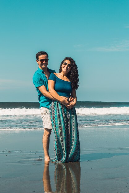 Glimlachende man en vrouw die op waterkant van strand koesteren
