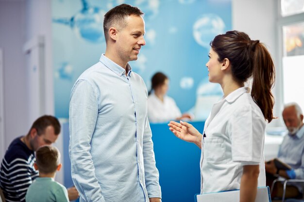 Glimlachende man en zijn vrouwelijke arts communiceren terwijl ze in een lobby van het ziekenhuis staan