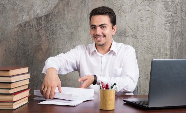 Glimlachende man met vellen papier en zittend aan het bureau. hoge kwaliteit foto