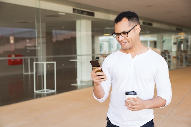 Glimlachende man texting op telefoon, afhaalmaaltijden koffie te houden