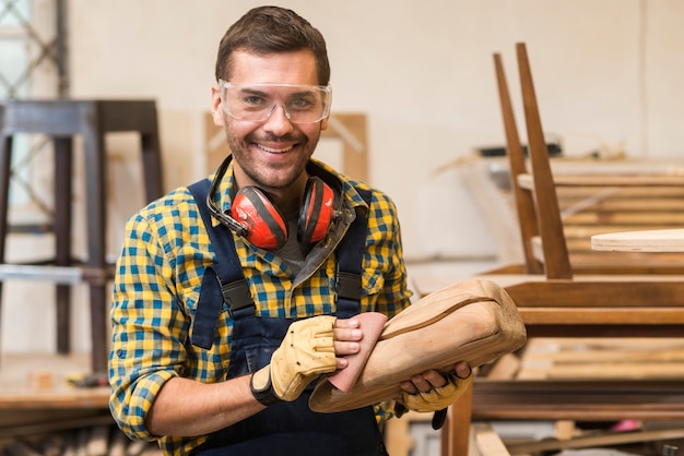 Glimlachende mannelijke timmerman die houten structuur met zanddocument gladstrijken