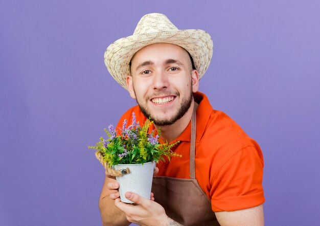 Glimlachende mannelijke tuinman die een tuinhoed draagt, houdt een bloempot vast