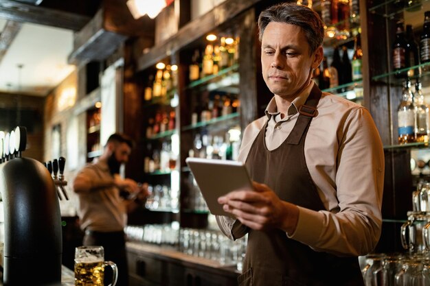 Glimlachende medio volwassen ober die touchpad gebruikt terwijl hij in een bar werkt