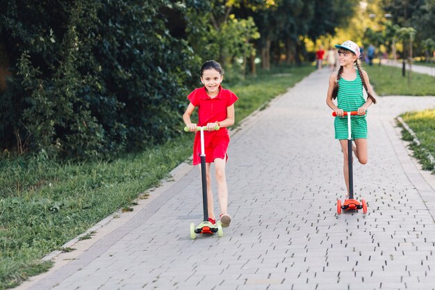 Glimlachende meisjes die op duwautoped over gang in het park berijden