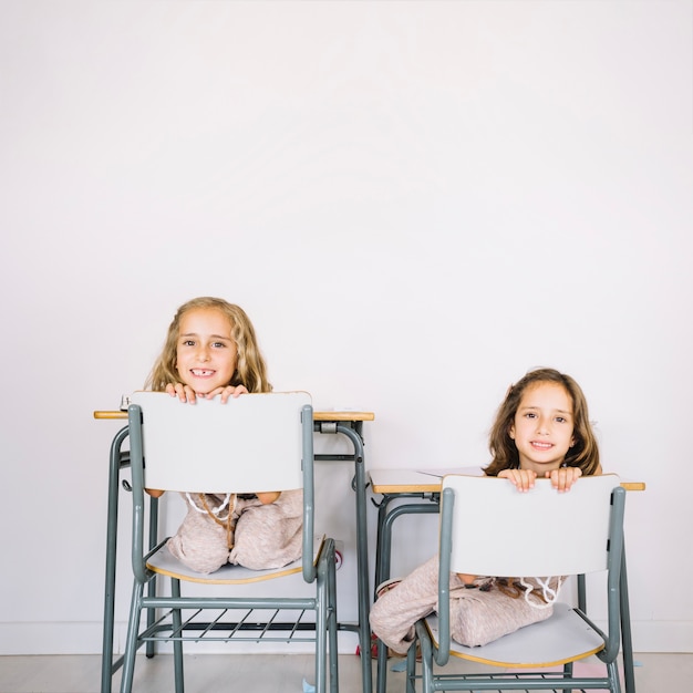 Glimlachende meisjes die van achter stoelen gluren