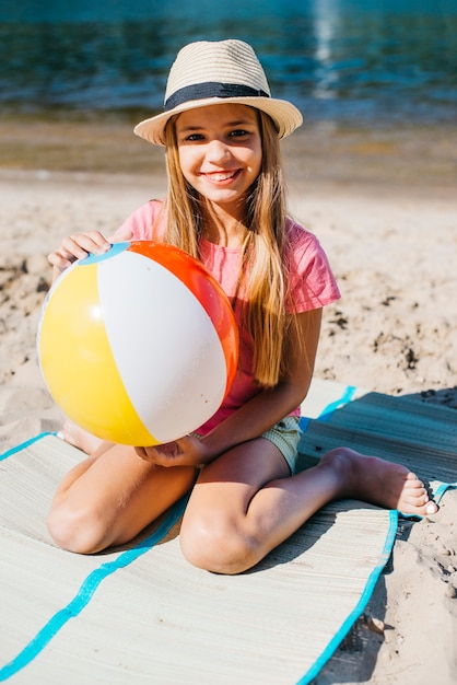 Glimlachende meisjeszitting met bal op strand