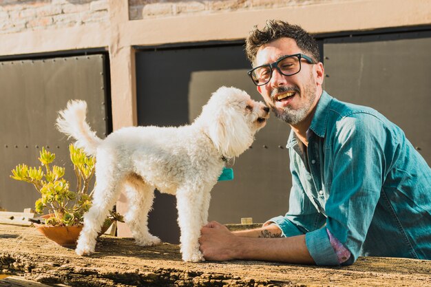 Glimlachende mens die oogglazen draagt die wit puppy spelen