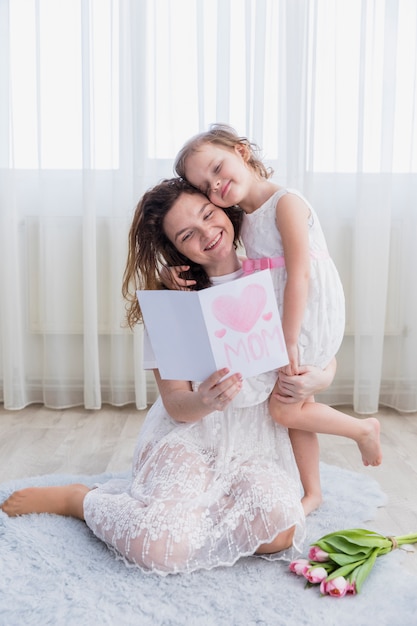 Glimlachende moeder en dochter de dagkaart van de lezingsmoeder samen thuis