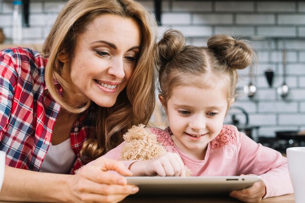 Glimlachende moeder en dochter die digitale tablet in keuken gebruiken