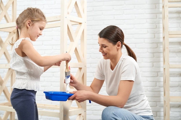 Glimlachende moeder en dochter die houten rek schilderen