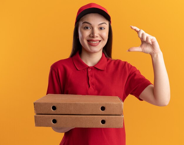 Glimlachende mooie bezorger in uniform met pizzadozen doet alsof ze iets vasthoudt