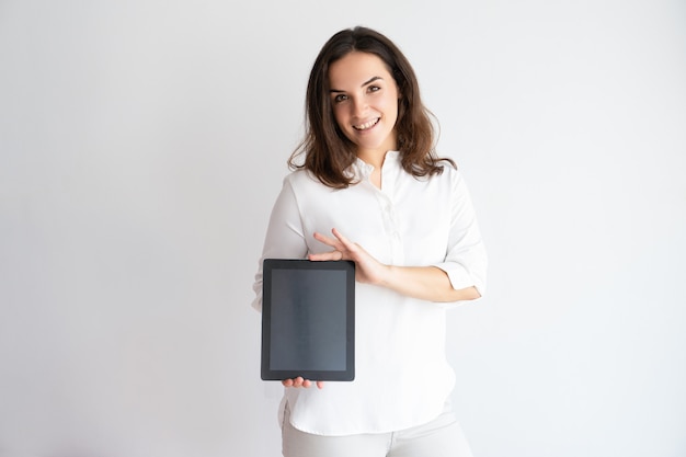 Glimlachende mooie de tabletcomputer van de vrouwenholding, die zijn het scherm toont en camera bekijkt.