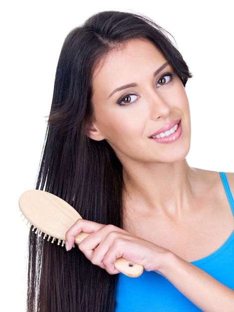 Glimlachende mooie jonge vrouw die haar lang bruin haar kamt met geïsoleerde haarborstel -