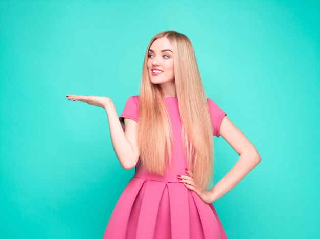 Glimlachende mooie jonge vrouw in het roze minikleding stellen, die iets voorstelt