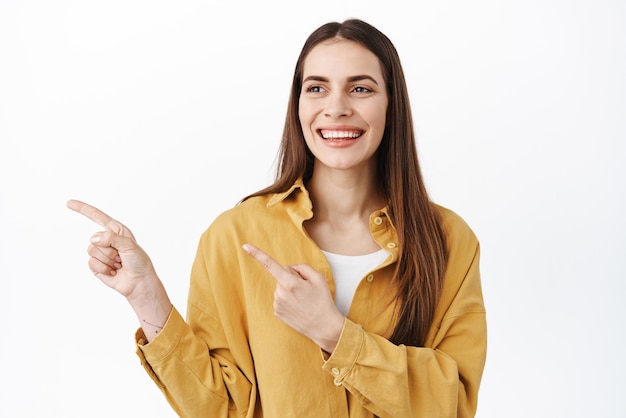 Glimlachende mooie vrouw draait het hoofd om en wijst naar links, ziet er blij en gelukkig uit om iets goeds te bekijken met een advertentielogo dat op een witte achtergrond staat