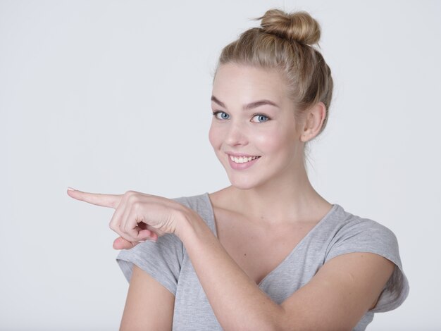 Glimlachende mooie vrouw wijzende vinger weg over grijze achtergrond. Kijkend naar de camera