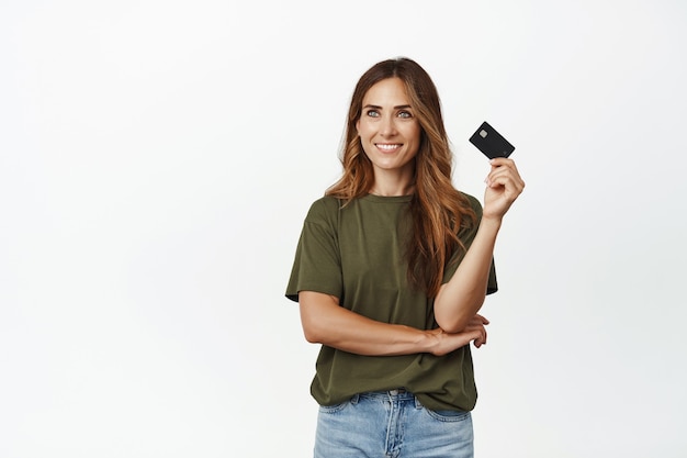 Glimlachende nadenkende vrouw die opzij kijkt, klaar om haar creditcard te gebruiken