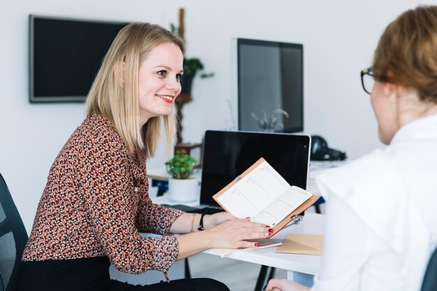 Glimlachende onderneemster die agenda toont aan haar collega