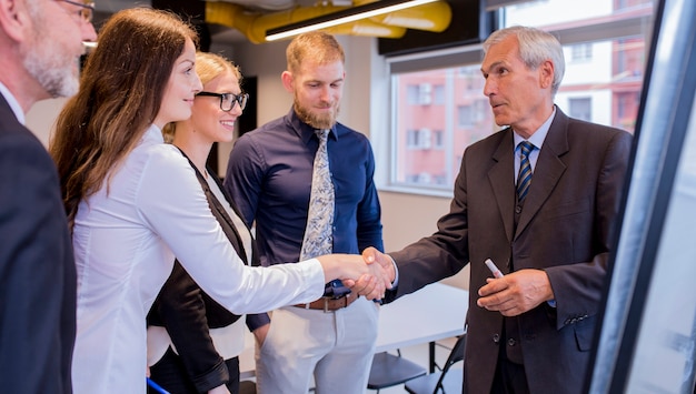 Glimlachende onderneemster het schudden hand met hogere zakenman in de raadsvergadering