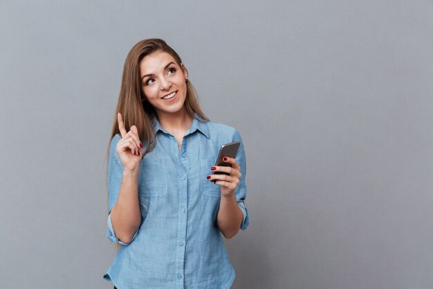 Glimlachende Peinzende Vrouw in overhemd dat telefoon met behulp van