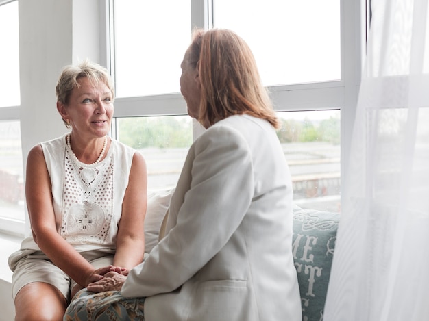 Gratis foto glimlachende rijpe vrouwenzitting met haar moeder op venstervensterbank