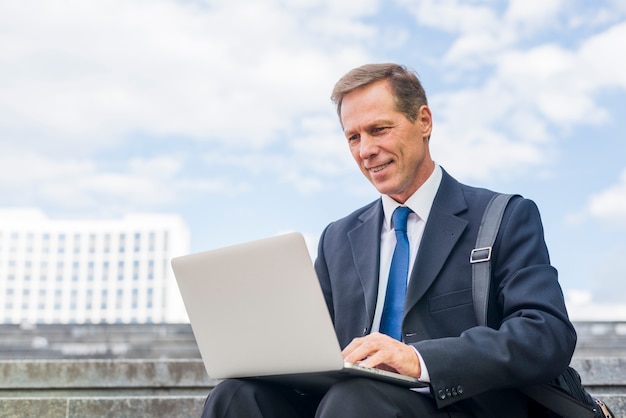 Glimlachende rijpe zakenman die laptop met behulp van bij openlucht