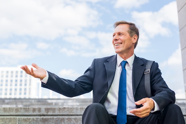 Glimlachende rijpe zakenmanzitting op trap die handgebaar maken