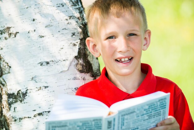 Glimlachende schooljongen die het boek in aard leest