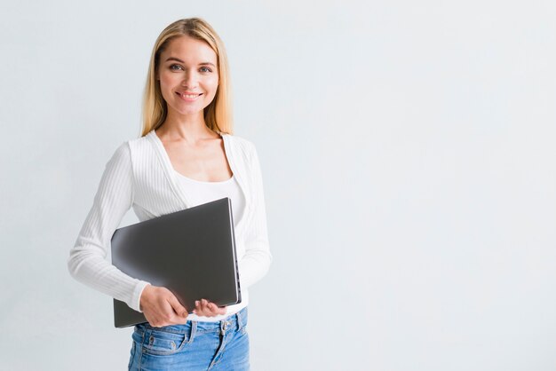 Glimlachende slanke blonde vrouw in jeans met zwarte laptop