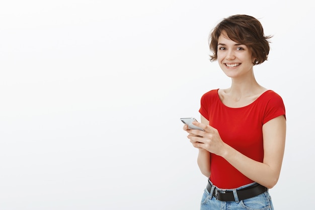 Glimlachende stijlvolle vrouw met behulp van mobiele telefoon, sms'en of browsen op sociale media