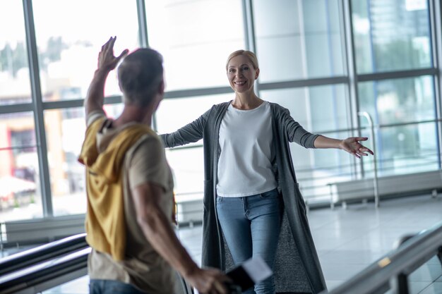 Glimlachende tevreden blonde vrouw in vrijetijdskleding die een mannelijke toerist ontmoet op de luchthaventerminal