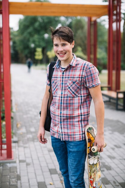 Glimlachende tiener met skateboard dichtbij boog