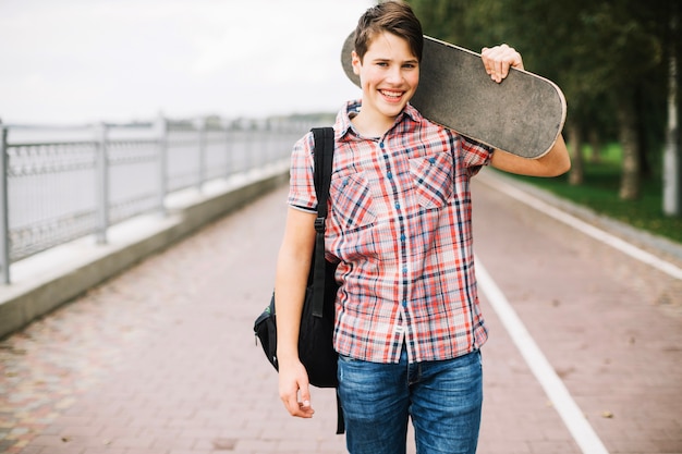 Gratis foto glimlachende tiener met skateboard op schouder