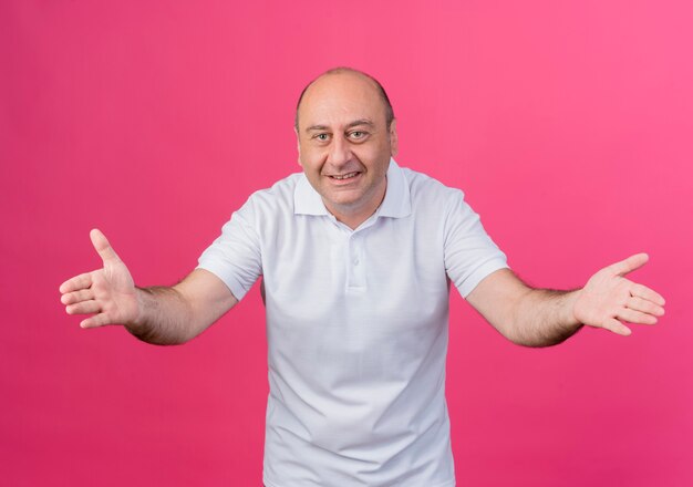 Glimlachende toevallige volwassen zakenman die lege handen toont die camera bekijken die op roze achtergrond wordt geïsoleerd